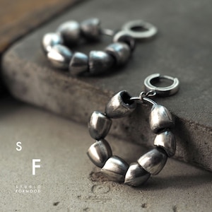 Könnte beinhalten: Ein Paar silberne Creolen mit einem runden Design aus kleinen, abgerundeten Perlen. Die Ohrringe sind aus Metall und haben einen schlichten, minimalistischen Stil.