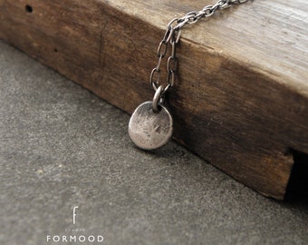 May include: A silver chain necklace with a small, round, textured pendant. The pendant is slightly hammered and has a rustic look.