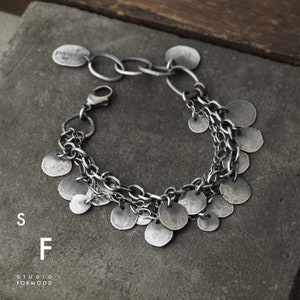 May include: A silver bracelet with multiple chains and dangling round charms. The charms are all different sizes and have a textured finish.