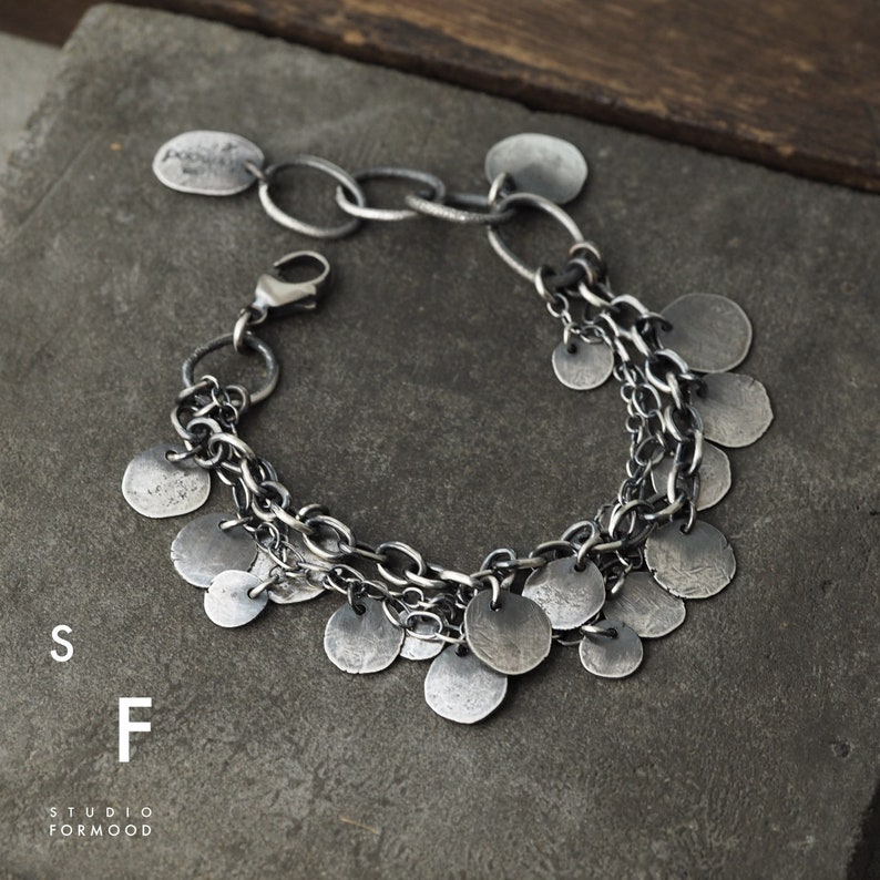 May include: A silver bracelet with multiple chains and dangling round charms. The charms are all different sizes and have a textured finish.