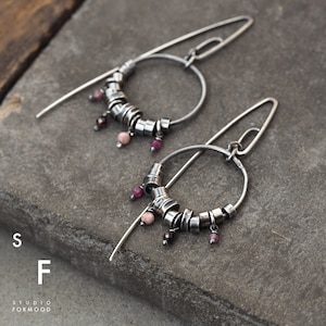 Peut inclure: Une paire de boucles d'oreilles créoles en argent avec un cercle de petites perles argentées et des pierres précieuses roses et rouges qui pendent du bas.