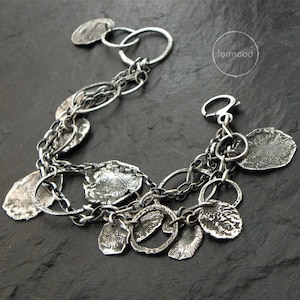 May include: A silver bracelet featuring multiple chain links and textured metal charms. The bracelet has a lobster clasp fastening. The word "formood" is visible in the image.