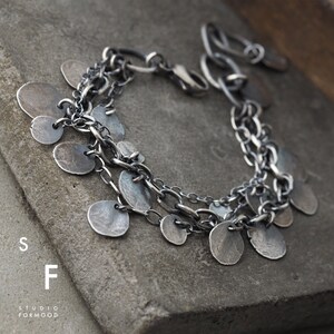 May include: A silver bracelet with multiple chains and dangling round charms. The bracelet has a clasp closure.