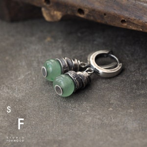 May include: A pair of silver earrings with green stone accents. The earrings feature a twisted silver design and a hoop closure.