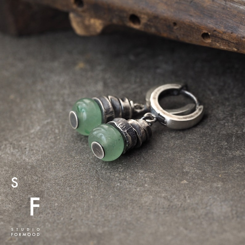 May include: A pair of silver earrings with green stone accents. The earrings feature a twisted silver design and a hoop closure.