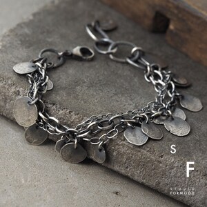 May include: A silver chain bracelet with multiple dangling silver discs. The bracelet has a lobster clasp closure. The bracelet is on a gray textured surface.  The text "STUDIO FORMOOD" is visible in the lower right corner of the image.
