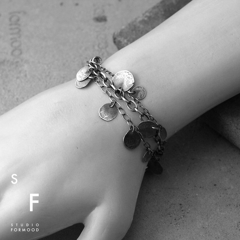 May include: A silver bracelet with multiple chains and small round charms. The bracelet is on a person's wrist.
