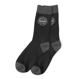 Peut inclure: Une paire de chaussettes noires avec un motif blanc qui dit "Le meilleur grand-père du monde".