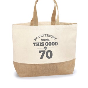 Puede incluir: Una bolsa de lona beige con ribete de yute marr&oacute;n. La bolsa tiene una impresi&oacute;n gris que dice "Not everyone looks this good at 70".