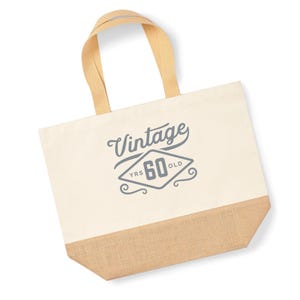 May include: A beige canvas tote bag with a brown jute bottom. The bag has a gray design that says "Vintage 60 YRS OLD" in a diamond shape.