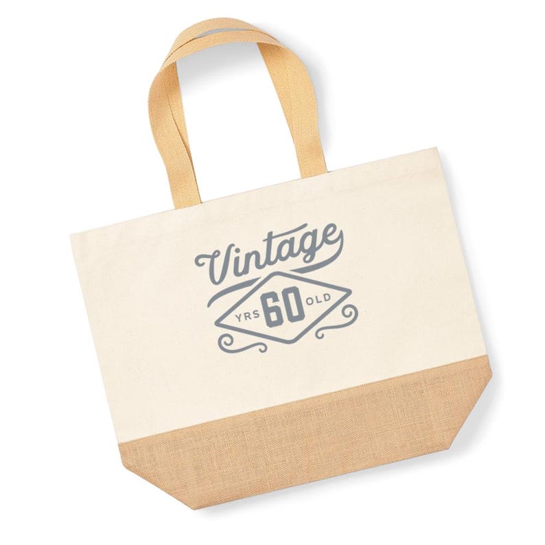 May include: A beige canvas tote bag with a brown jute bottom. The bag has a gray design that says "Vintage 60 YRS OLD" in a diamond shape.
