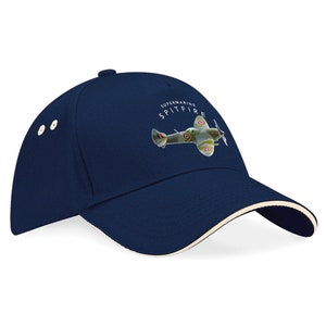 May include: A navy blue baseball cap with a white brim. The cap features a white graphic of a Supermarine Spitfire airplane with the text "Supermarine Spitfire" above it.