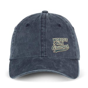 Op de afbeelding: Een antracietgrijze honkbalpet met een verwassen afwerking. De voorkant is voorzien van geborduurde tekst in crème en donkerblauw met de tekst "WORLD'S No.1 Grumps" en een klein sterretje, gecentreerd boven de gebogen klep van de pet.