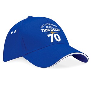 May include: Blue baseball cap with a white brim and white text that reads "Not everyone looks this good at 70".