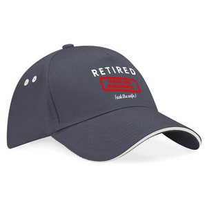 May include: A navy blue baseball cap with a white brim. The front of the cap has white text that reads "RETIRED" and a red stamp that says "Officially Retired From Management" with the text "(ask the wife)" below the stamp.