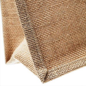 Puede incluir: Primer plano de la costura de una bolsa de mano de yute marr&oacute;n natural. La tela est&aacute; tejida con una textura rugosa.