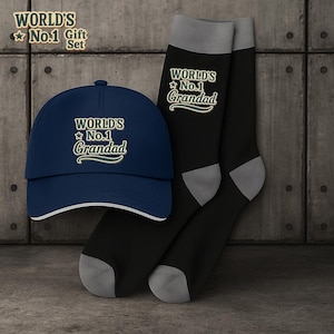 Op de afbeelding: Een cadeau set met een marineblauwe baseball cap en zwarte sokken. De tekst "WORLD'S No.1 Grandad" is in wit en groen. De cap heeft een witte rand. De sokken hebben grijze hielen en tenen. De tekst "WORLD'S No.1 Gift Set" is ook zichtbaar.
