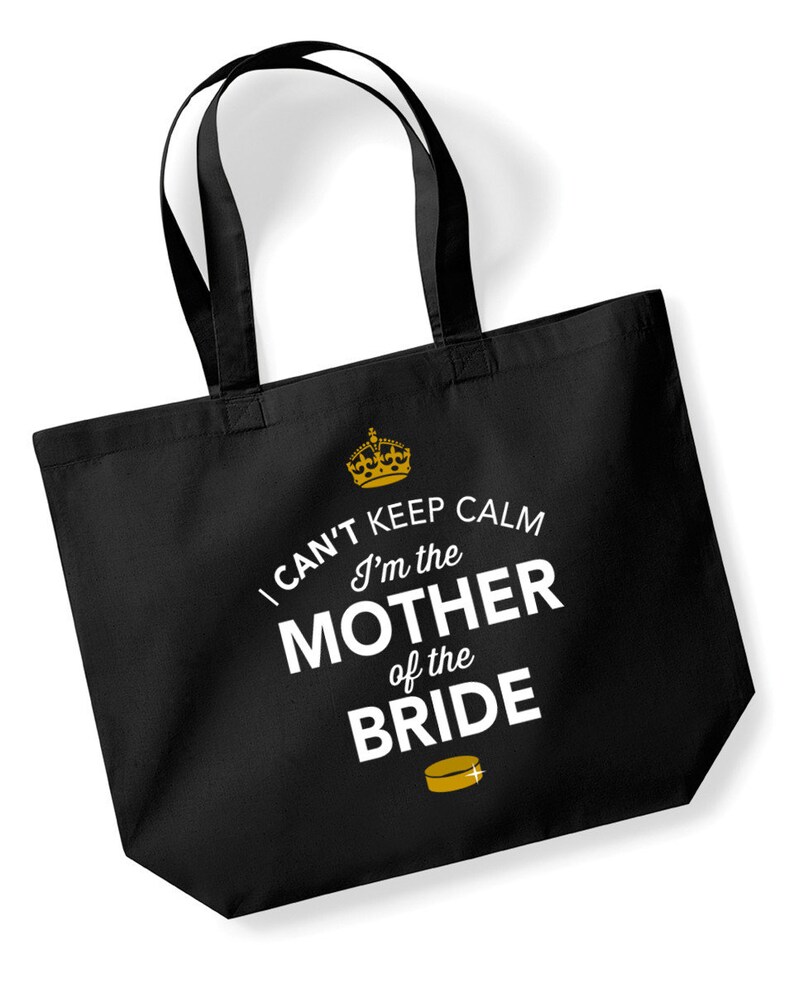 Puede incluir: Bolsa de tela negra con una corona dorada y el texto "I can't keep calm I'm the Mother of the Bride" en blanco. Un disco de hockey dorado se encuentra debajo del texto.