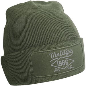 May include: An olive green knitted beanie hat with a rectangular patch. The patch displays the word "Vintage" above the year "1966" in a diamond shape, in light grey. A winter hat.