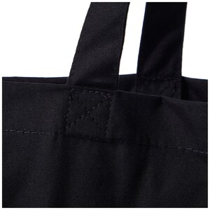 Puede incluir: Primer plano de las asas de una bolsa de lona negra, mostrando el detalle de la costura.