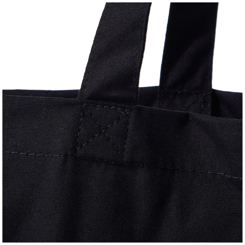 Puede incluir: Primer plano de las asas de una bolsa de lona negra, mostrando el detalle de la costura.