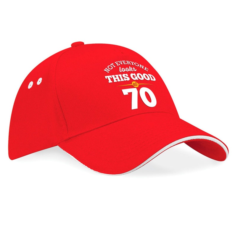 May include: Red baseball cap with a white brim and white text that reads "Not everyone looks this good at 70".
