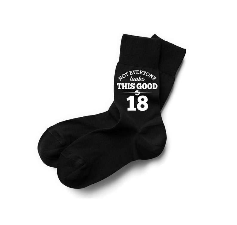 Puede incluir: Un par de calcetines negros con el texto blanco "NOT EVERYONE looks THIS GOOD at 18". Los calcetines est&aacute;n hechos de un material suave y est&aacute;n dise&ntilde;ados para usarse en los pies.