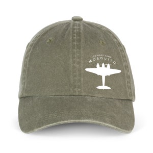 Op de afbeelding: Een groene katoenen baseballpet met een wit silhouet van een De Havilland Mosquito vliegtuig en de tekst "DE HAVILLAND MOSQUITO" op de voorkant.