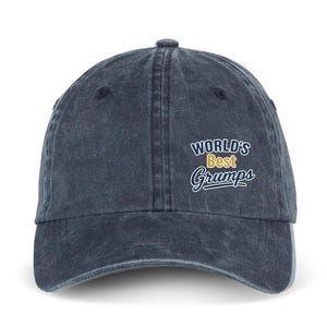 Op de afbeelding: Een donkerblauwe baseballpet van verwassen denim met de geborduurde tekst "WORLD'S Best Grumps" op de voorkant. De pet heeft een gebogen klep, een knoop aan de bovenkant en gestikte oogjes voor ventilatie, wat zorgt voor een gedragen uitstraling.