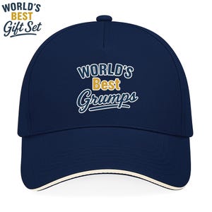 Op de afbeelding: Een marineblauwe baseballcap met witte rand en de tekst "WORLD'S Best Grumps" in witte en gouden letters. De zin "WORLD'S BEST Gift Set" is ook zichtbaar. Een klassiek, casual accessoire.