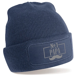 Può includere: Un berretto blu navy con una toppa grigia che dice "No.1 PAPA" con un baffo grigio sotto.