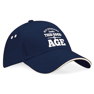 May include: A navy blue baseball cap with a white brim and the text "Not everyone looks this good at age" in white.