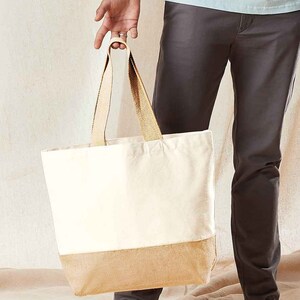 May include: A white canvas tote bag with a brown burlap bottom. The bag has two brown straps and is being held by a person.