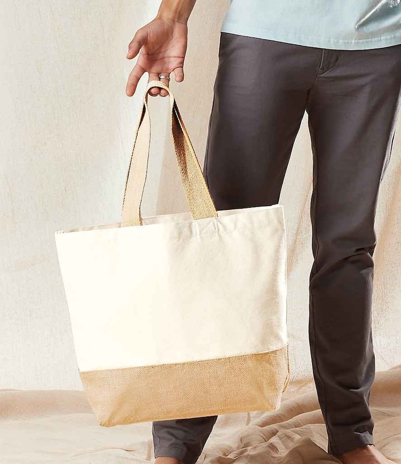 May include: A white canvas tote bag with a brown burlap bottom. The bag has two brown straps and is being held by a person.