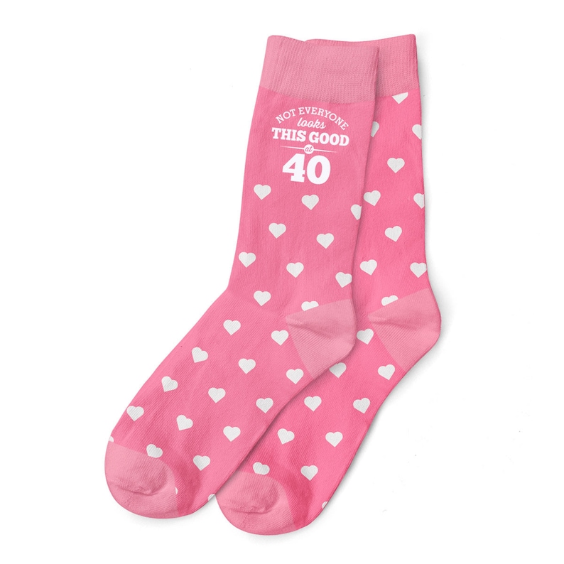 May include: Pink socks with a white heart pattern. The socks have a white text graphic that reads "Not everyone looks this good at 40".