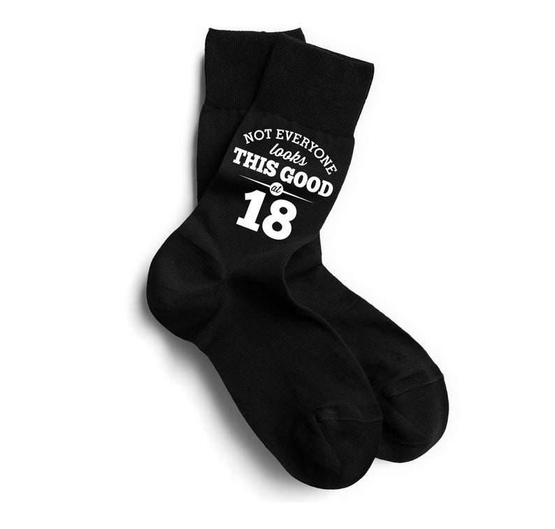 Puede incluir: Un par de calcetines negros con el texto blanco "NOT EVERYONE looks THIS GOOD at 18". Los calcetines se muestran sobre un fondo blanco.