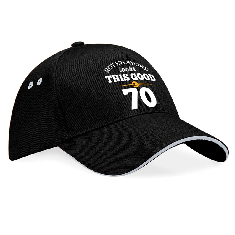 May include: Black baseball cap with a white brim and white text that reads "Not everyone looks this good at 70".