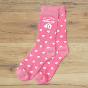 May include: Pink socks with white hearts and the text "Not everyone looks this good at 40".