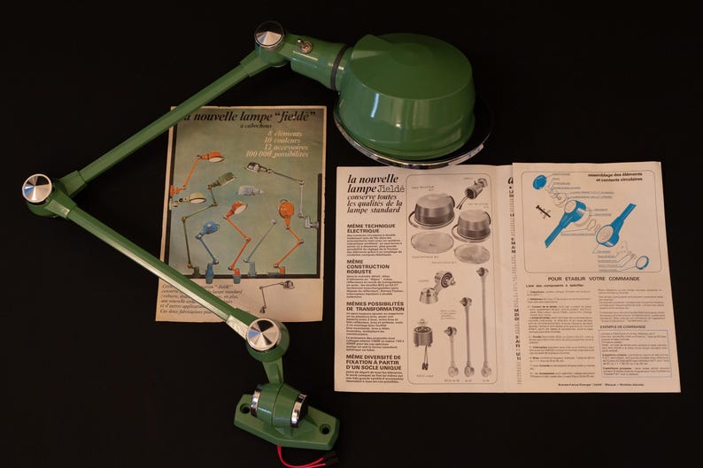 May include: A green metal desk lamp with a flexible arm and a round shade. The lamp is shown with its instruction manual, which includes the text "la nouvelle lampe "field"  con&ccedil;ue pour toutes les applications de la lampe standard".
