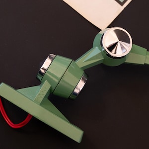 May include: A green metal lamp with a chrome accent and a red wire. The lamp has a swivel arm and a base that can be mounted to a surface.
