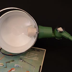 May include: A green and chrome desk lamp with a white interior shade. The lamp is adjustable and has a long arm. The lamp is on a box with the text "Jield&eacute;" and information about the lamp's features.