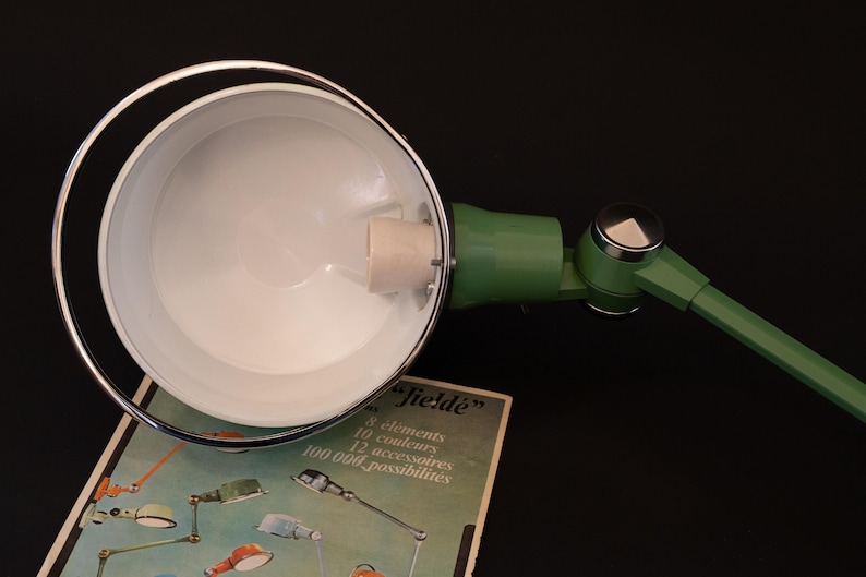 May include: A green and chrome desk lamp with a white interior shade. The lamp is adjustable and has a long arm. The lamp is on a box with the text "Jield&eacute;" and information about the lamp's features.