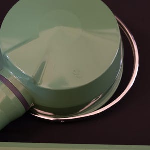 May include: A green metal lamp with a silver ring around the top. The lamp has a round, dome-shaped shade.