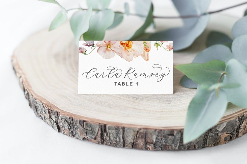 Peut inclure: Une carte de table blanche avec un motif floral compos&eacute; de fleurs roses et orange. Le texte "Carla Ramsey" et "Table 1" est imprim&eacute; en noir.
