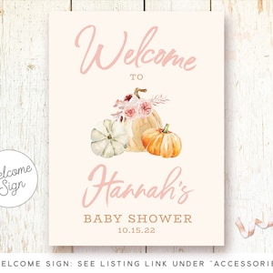 May include: Welcome sign for a baby shower with a pink background and a watercolor illustration of pumpkins and flowers. The text reads "Welcome to Hannah's Baby Shower 10.15.22".