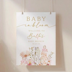 Może przedstawiać: Prostokątny biały znak ze złotym tekstem i ilustracjami kwiatowymi. Tekst brzmi "BABY in bloom" i "WELCOME TO Bella's BABY BRUNCH 08.20.XX". Na dole znaku znajdują się kwiaty w stylu akwareli w odcieniach r&oacute;żu, brzoskwini i fioletu.