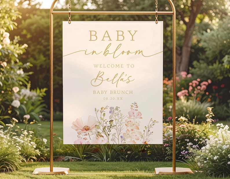 Może przedstawiać: Złota metalowa rama trzyma znak z napisem "BABY in bloom" i "Welcome to Bella's BABY BRUNCH 08.20.XX". Znak zawiera kwiatowe ilustracje w miękkich r&oacute;żach i fioletach na jasnym tle.