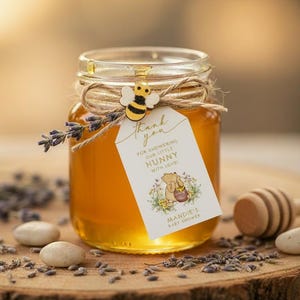 May include: A clear glass jar filled with golden honey, tied with twine and a small wooden bee charm. A white tag attached reads: Thank you for showering our little hunny with love! Mandie's baby shower, featuring a bear illustration.