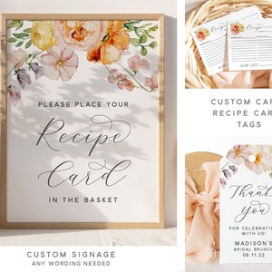 Peut inclure: Une affiche imprimable avec des illustrations florales aquarelle et le texte "Veuillez placer votre carte de recette dans le panier". L'affiche est encadr&eacute;e dans un cadre en bois clair. L'affiche fait partie d'un ensemble de d&eacute;corations de f&ecirc;te de mariage imprimables qui comprend &eacute;galement des cartes de recettes et des &eacute;tiquettes de remerciement.