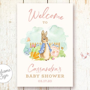 May include: Welcome to Cassandra's Baby Shower sign with a watercolor illustration of a rabbit in a blue jacket, carrots, flowers, and a fence. The date of the shower is 03.17.20.